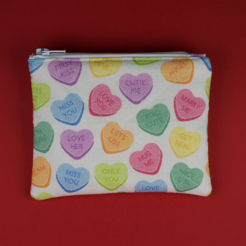 Fabric pouch with colorful heart-shaped designs on a red background
